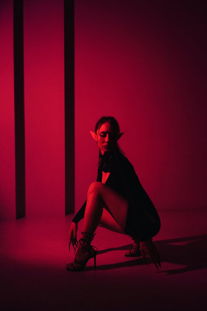 A woman in black clothing with elf ears kneels dramatically under red lighting, conveying a mystical ambiance.